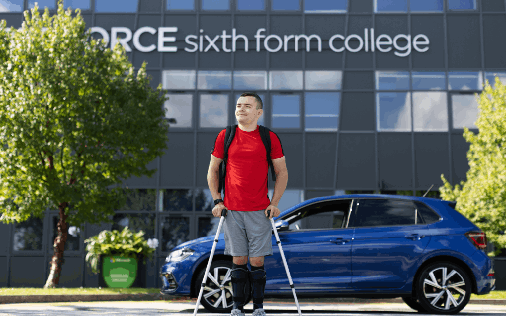 A young man is walking away from his blue vehicles using crutches. He had a red top on with a black backpack and blue shorts. He is looking away from the camera. Behind him are the words "sixth form college" in letters across a grey large building.