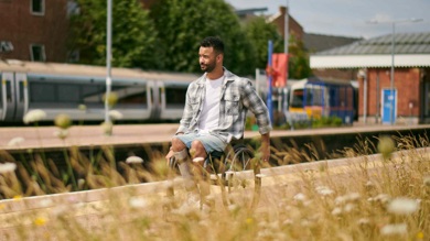 The photo is of a man in a wheelchair wheeling across a train station platform. 