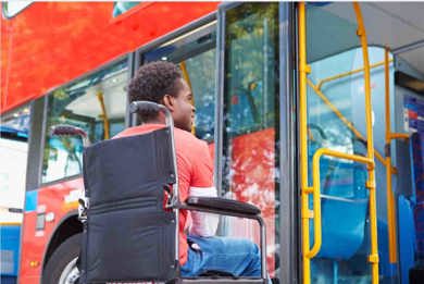 A man is sitting in a wheelchair in front of a bus. 