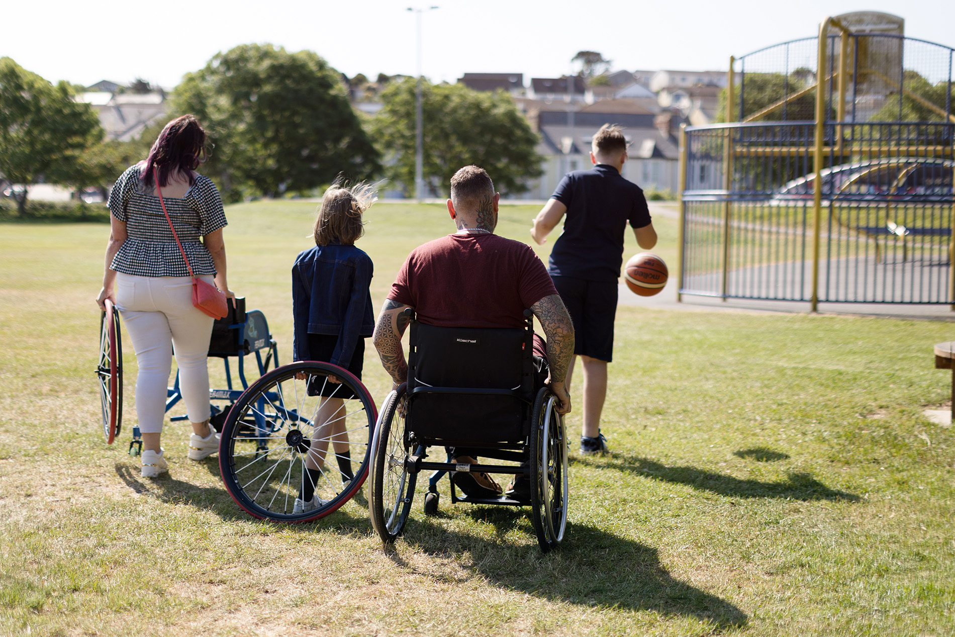 A man in a wheelchair and his family walk across a park