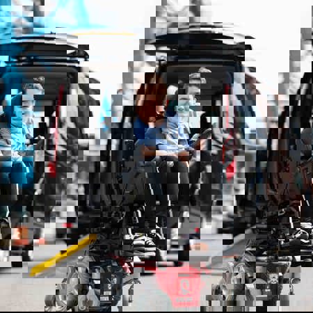 A boy in a wheelchair is next to a car.
