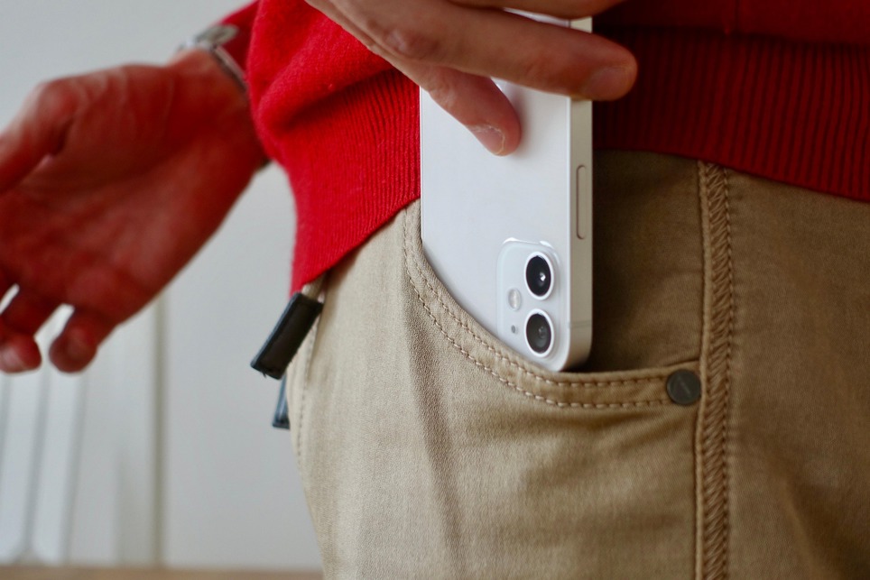 The back of a white iPhone 12 smartphone being placed in a pocket. You can see the two cameras.