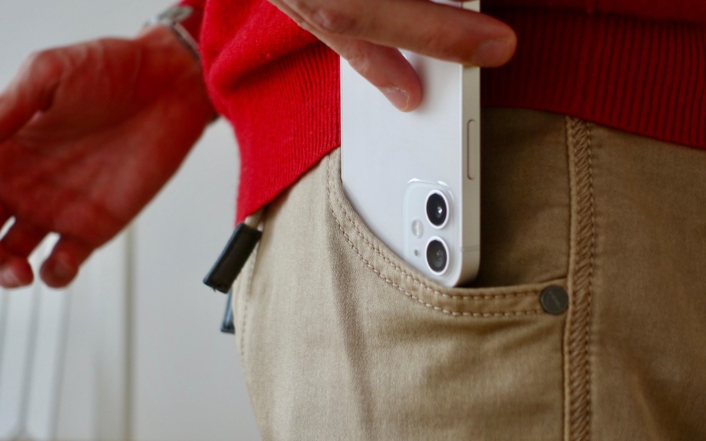 The back of a white iPhone 12 smartphone being placed in a pocket. You can see the two cameras.