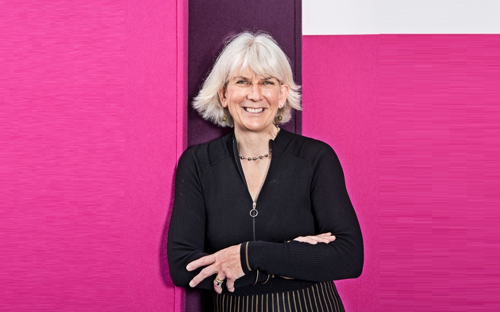 Kate is smiling and wearing a black top and gold and black striped skirt.