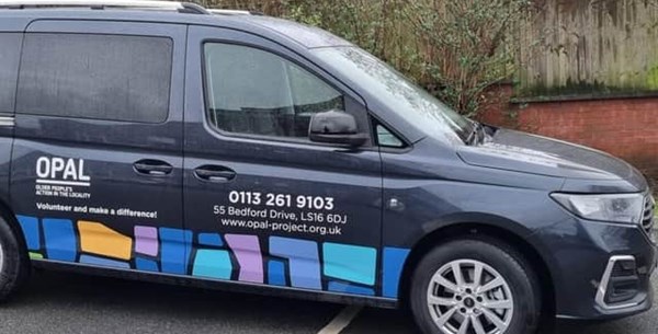 An image of OPAL's wheelchair accessible vehicle. The vehicle is black and has their logo and telephone number on the side.