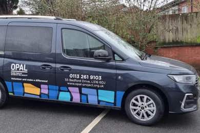 An image of OPAL's wheelchair accessible vehicle. The vehicle is black and has their logo and telephone number on the side.