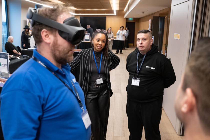 A man is wearing a blue polo shirt and black goggles. A man facing away from the camera is talking to a women and man in front of him.