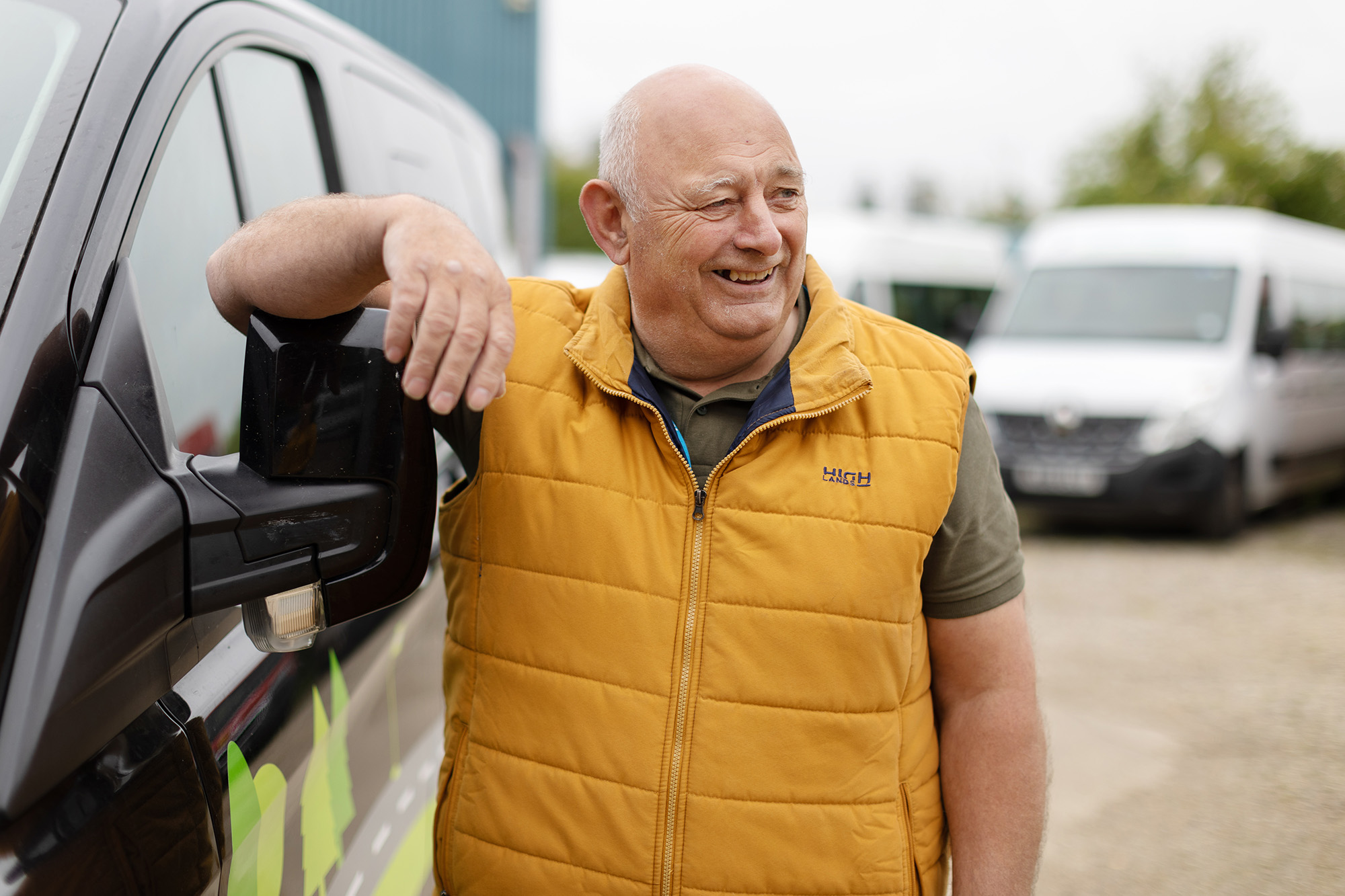 A smiling man wearing a yellow vest stands next to a wheelchair accessible vehicle with his arm placed on the mirror
