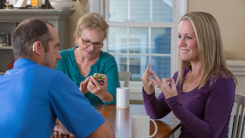 A man and a women sat at a wooden table with a British Sign Language interpreter. 