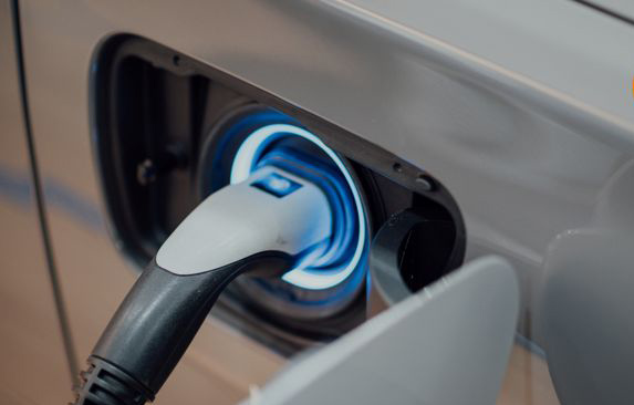 A silver electric vehicle with a charging-point plug charging up the vehicle.