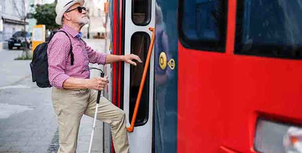 A man using a white cane climbing into the open door on a bus