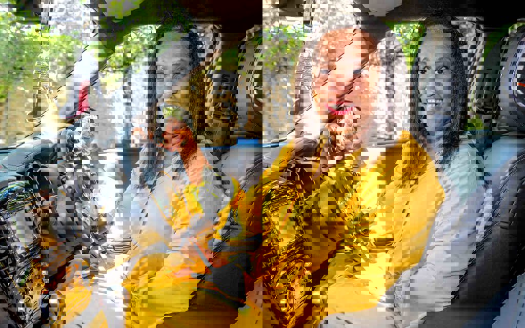 Allison is in a yellow outfit, sitting in the driving seat of her specially adapted car, with her hand on the wheel