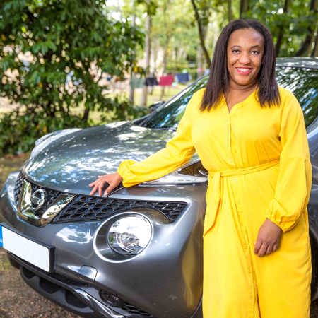 Allison has a big smile as she stands outside of her car leaning on the side of the bonnet