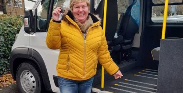 Lady smiling and proudly holding out the keys to a community transport vehicle, which is behind her. 