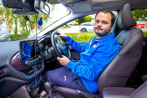 A gentleman is sitting in his car, wearing a bright blue jacket.