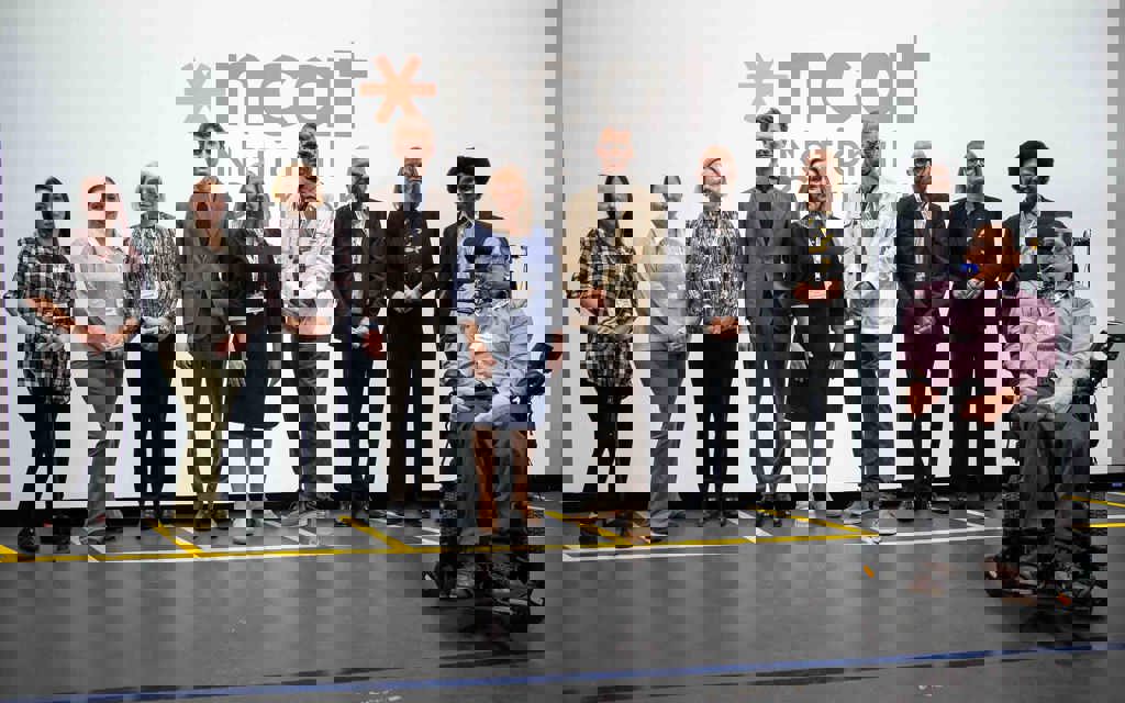 A group photo smiling in front of the NCAT logo which sits on a presentation backdrop. Caption left to right: Stephanie McPherson-Brown, Kay Atkin, Emily Nash, Robert McLaren, Cathryn Thompson-Goodwin, Professor Paul Herriotts, Gordon McCullough, Catharine Brown, Michael Edwards, Clive Gilbert