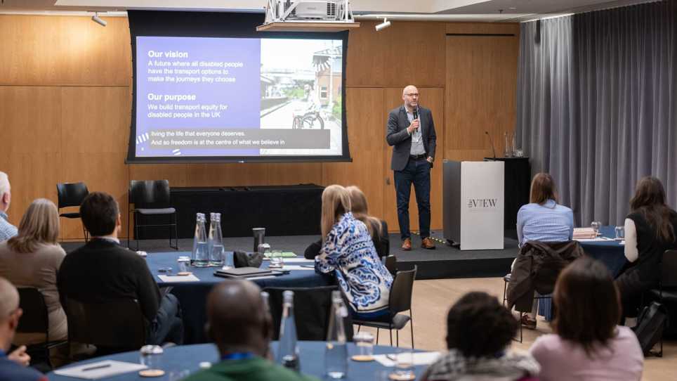 Nigel Fletcher, CEO is presenting at the front of an audience.   