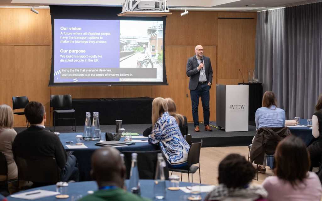 Nigel Fletcher, CEO is presenting at the front of an audience.   